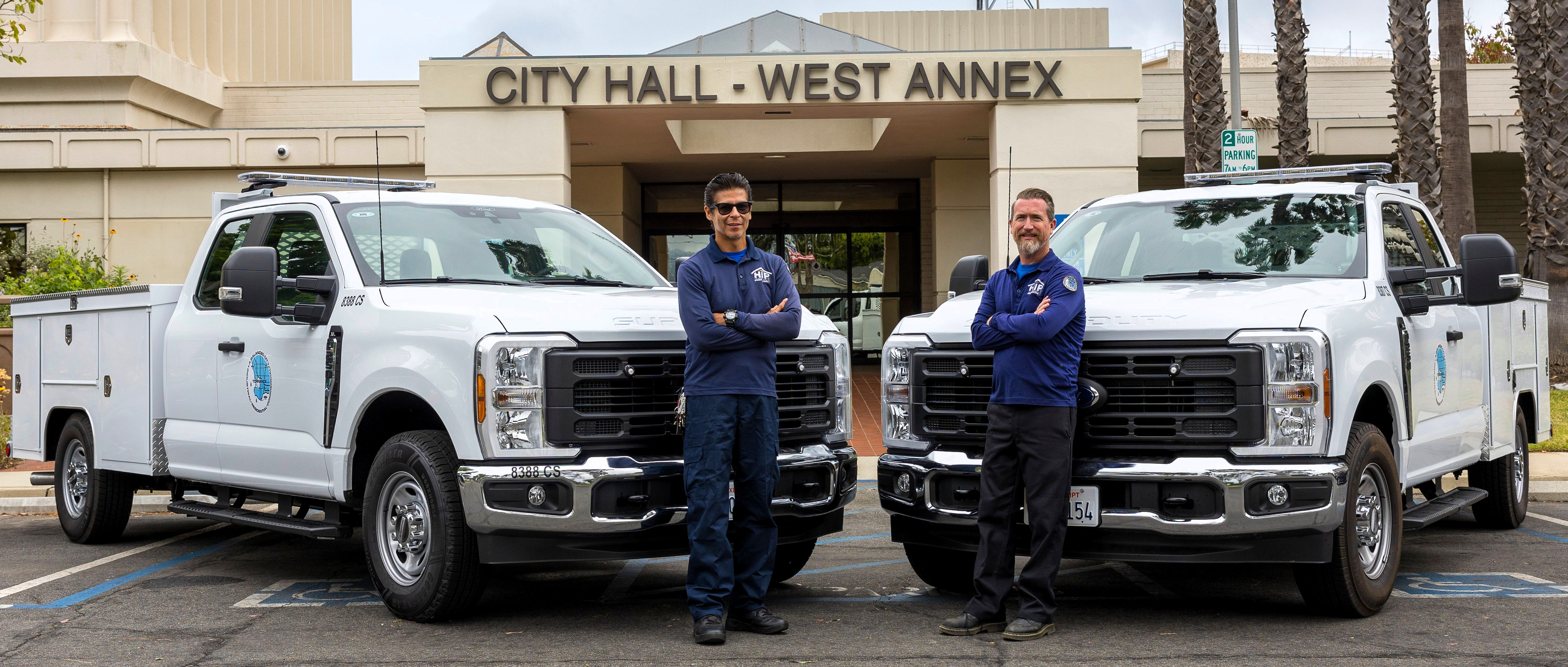 Home Improvement Program staff posing by their work trucks that are parked in front of the West Annex.