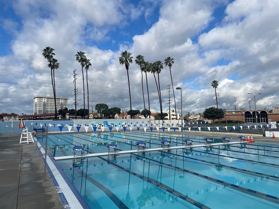 Olympic-size outdoor swimming pool with marked lanes and blue water and clouds