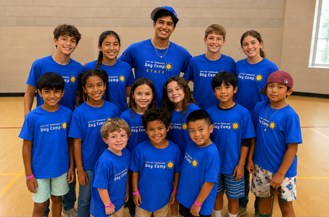 Smiling day camp children and recreation staff in matching blue camp shirts posing together in gymnasium. 