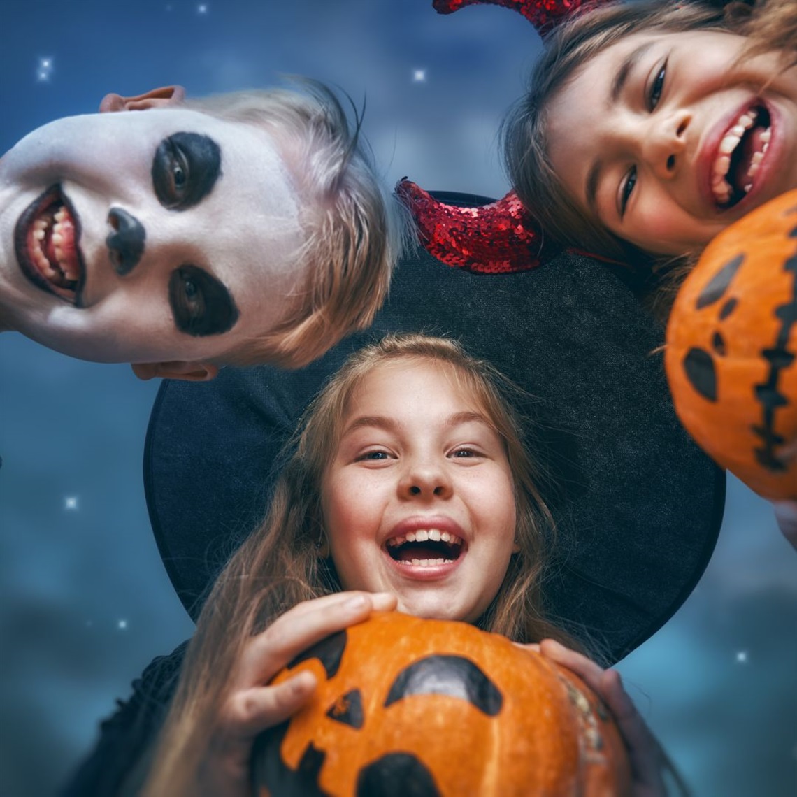Children in Halloween costumes looking down at the camera, smiling and gathered closely together.