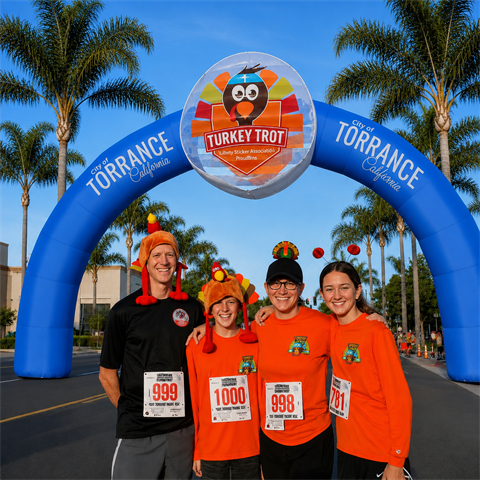 Four smiling participants pose beneath the City of Torrance Turkey Trot arch.