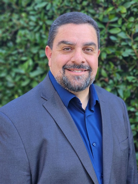 Professional headshot of Shant Megerdichian smiling in front of a leafy green background.